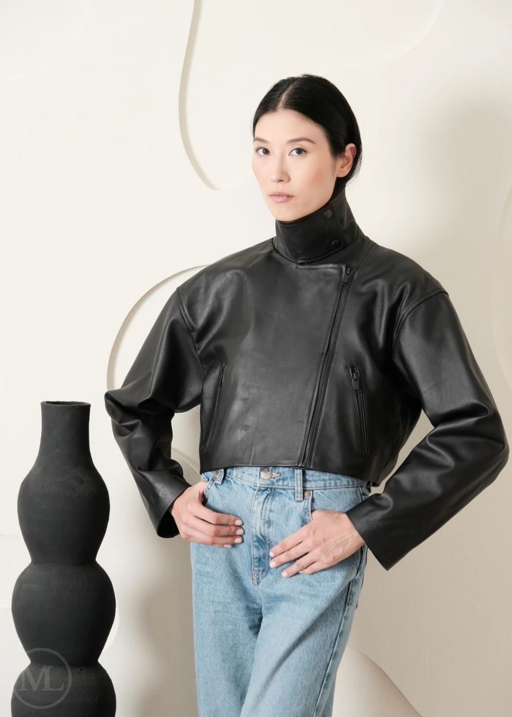 Women wearing a black leather Biker jacket and blue jeans standing against a plain backgroundn