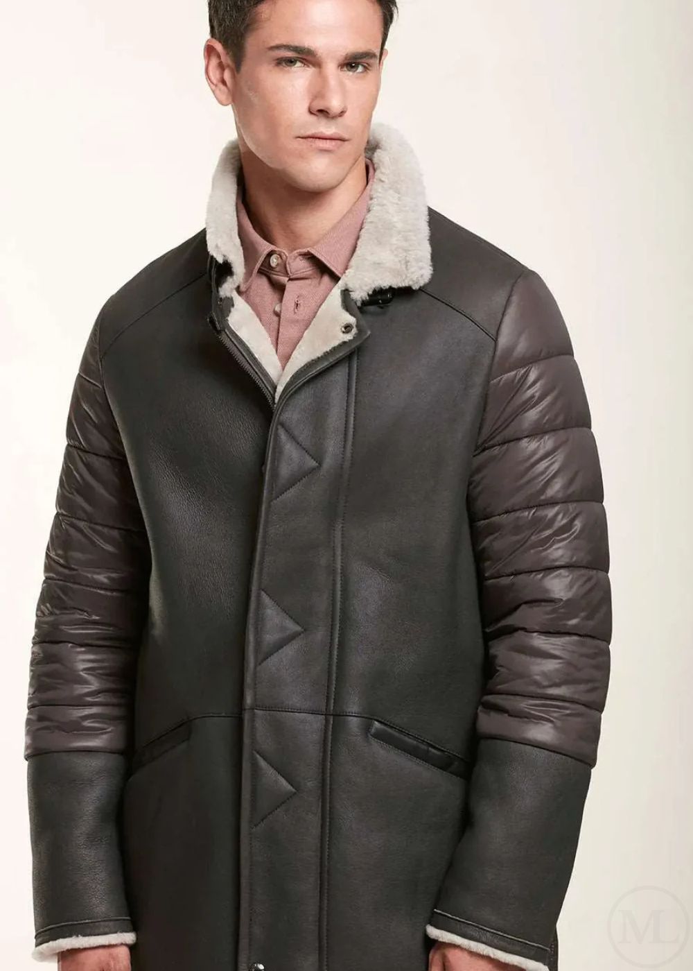 Man wearing a brown shearling leather jacket with white fur lining on a light background