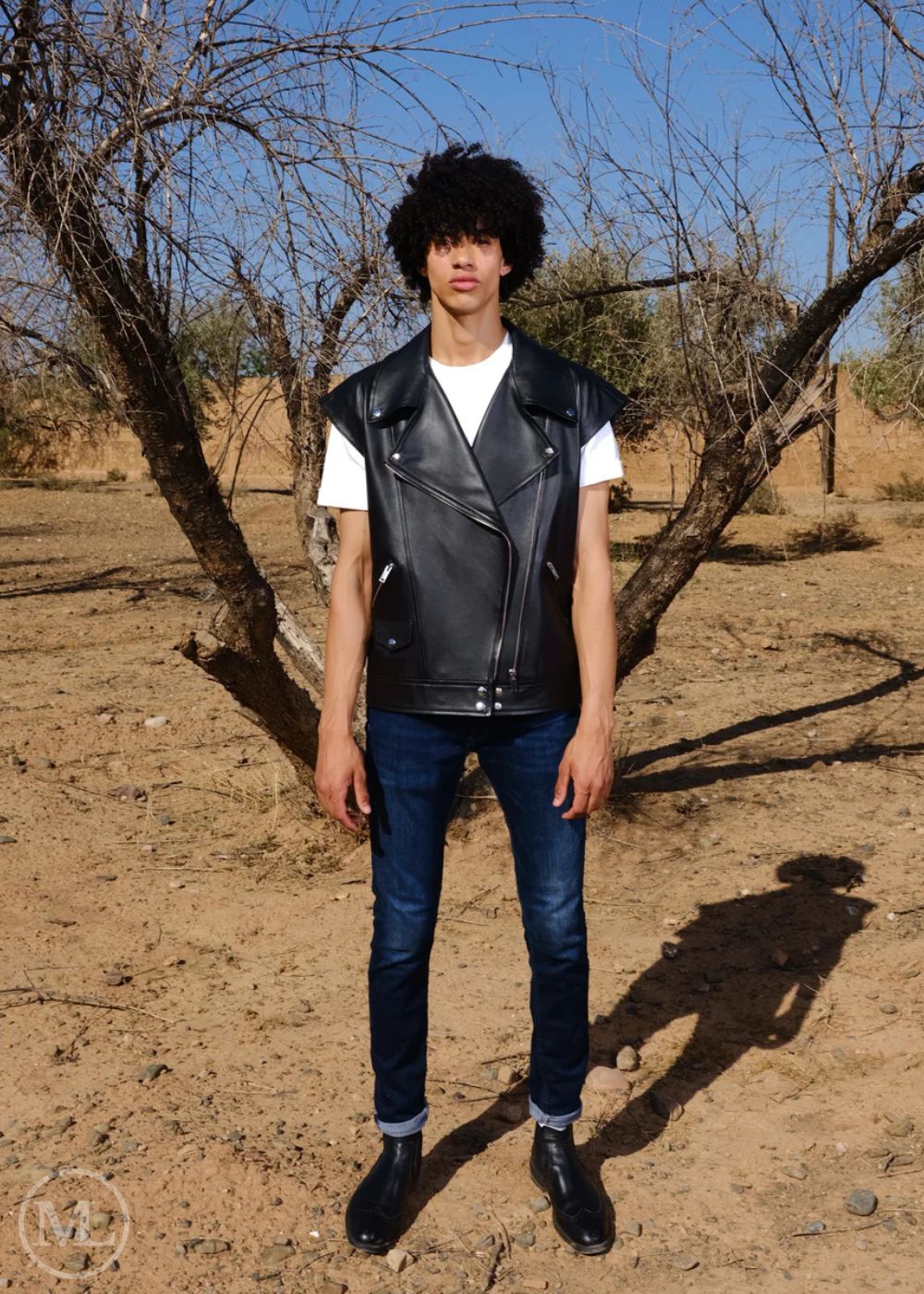 Women wearing a black leather vest, white shirt, and blue jeans standing in a desert-like environment.