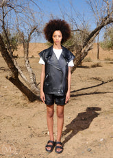Women wearing a black leather vest and shorts standing in a desert-like environment.
