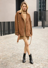 Woman wearing a Caramel brown leather biker jacket and dress with black boots on a city street.