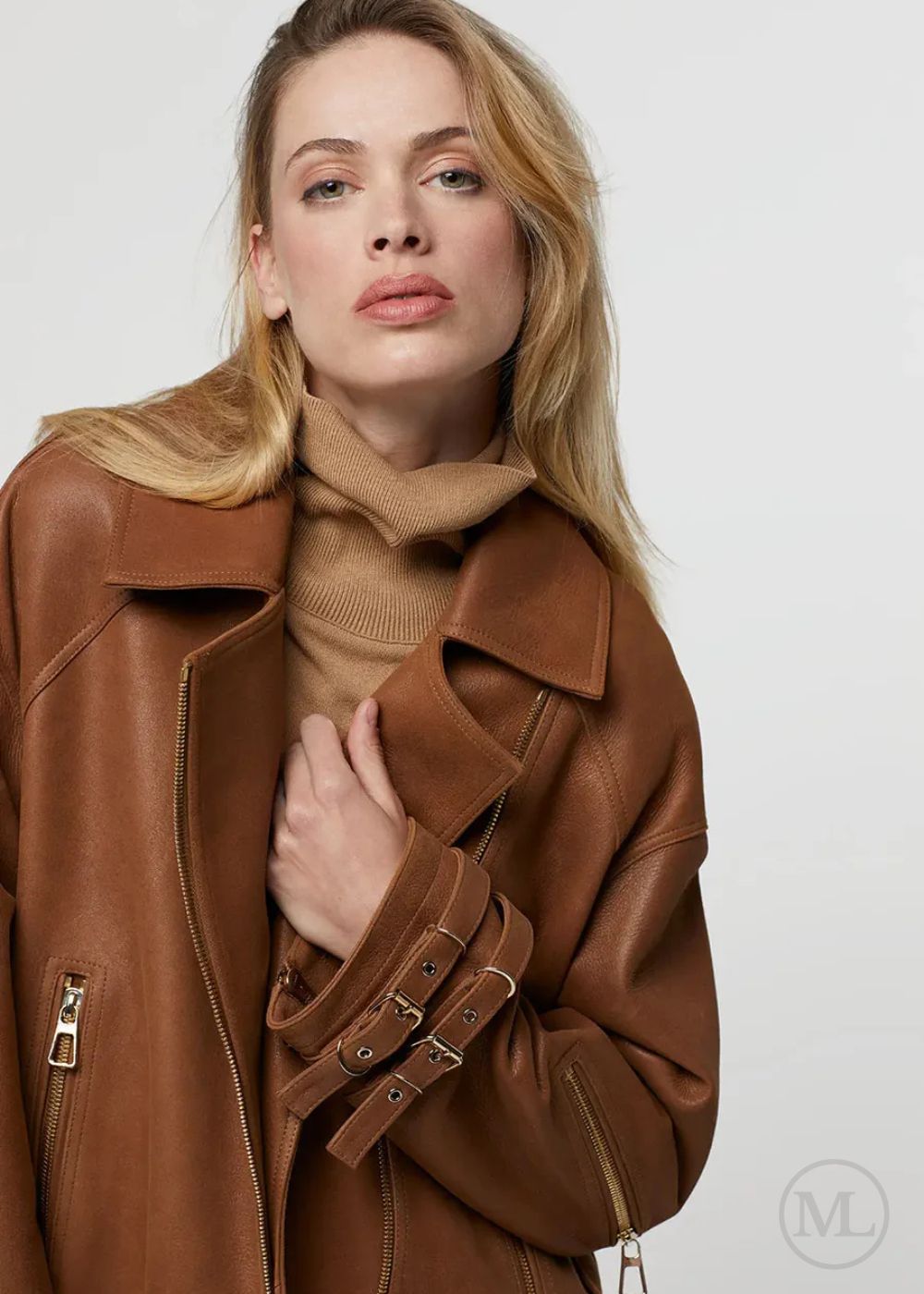 Femme portant une veste de motard en cuir marron caramel sur un pull à col roulé beige sur fond blanc