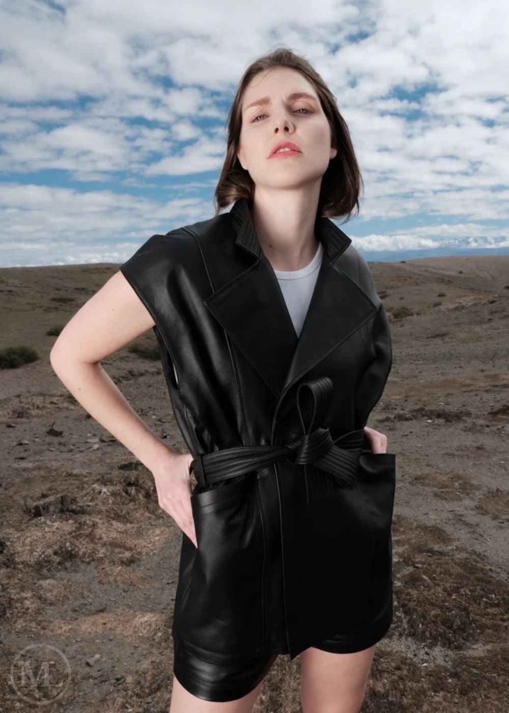 Woman wearing a black leather vest romper against a desert landscape with blue sky.