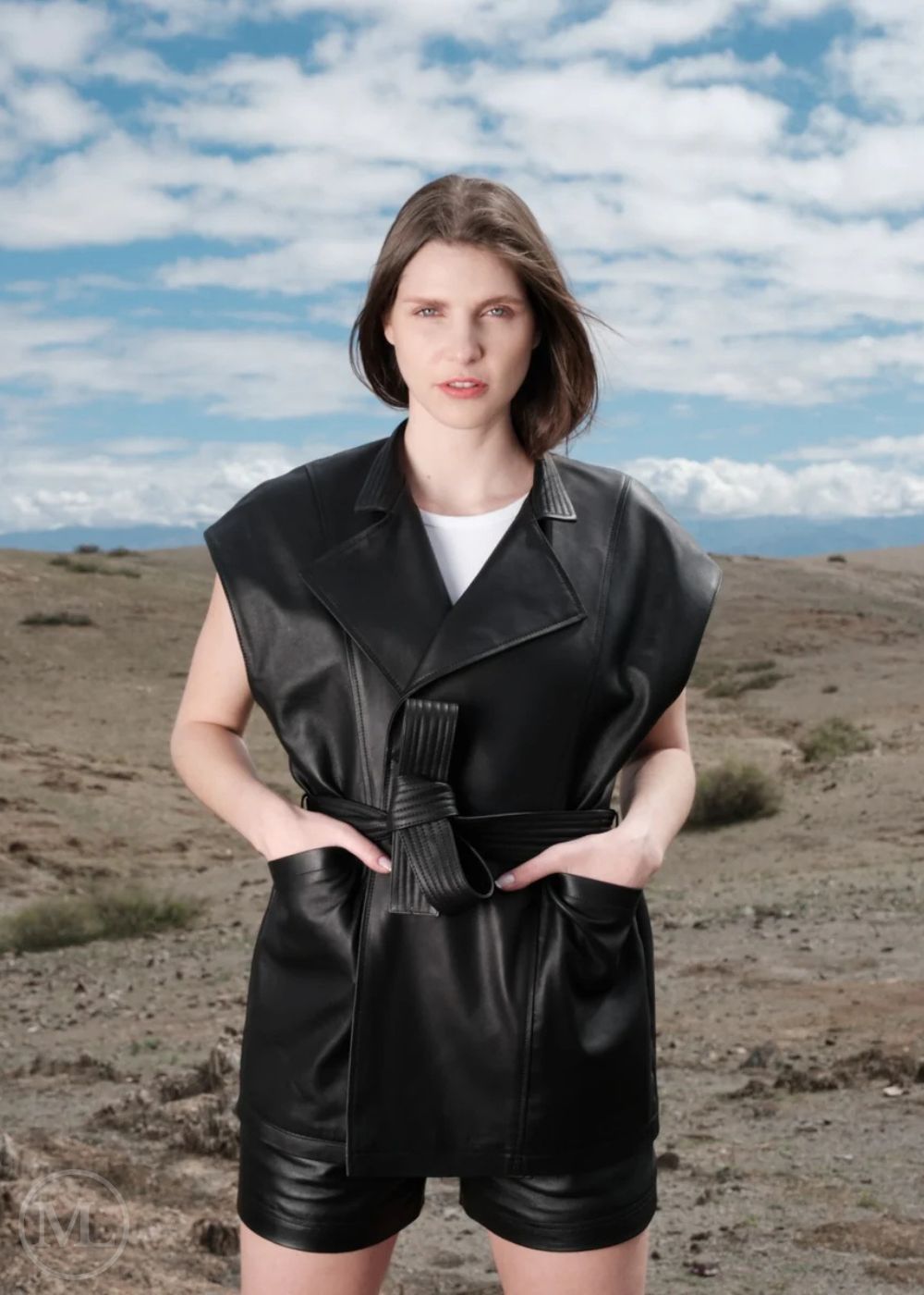 Woman wearing a black leather vest outfit against a desert landscape with blue sky.