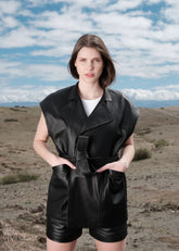 Woman wearing a black leather vest outfit against a desert landscape with blue sky.