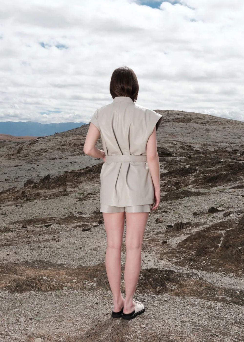 Women wearing a lvory romper standing on a rocky landscape with clouds in the sky