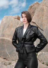 Woman wearing a black leather Blazer Coat outfit standing against rocky terrain with blue sky.