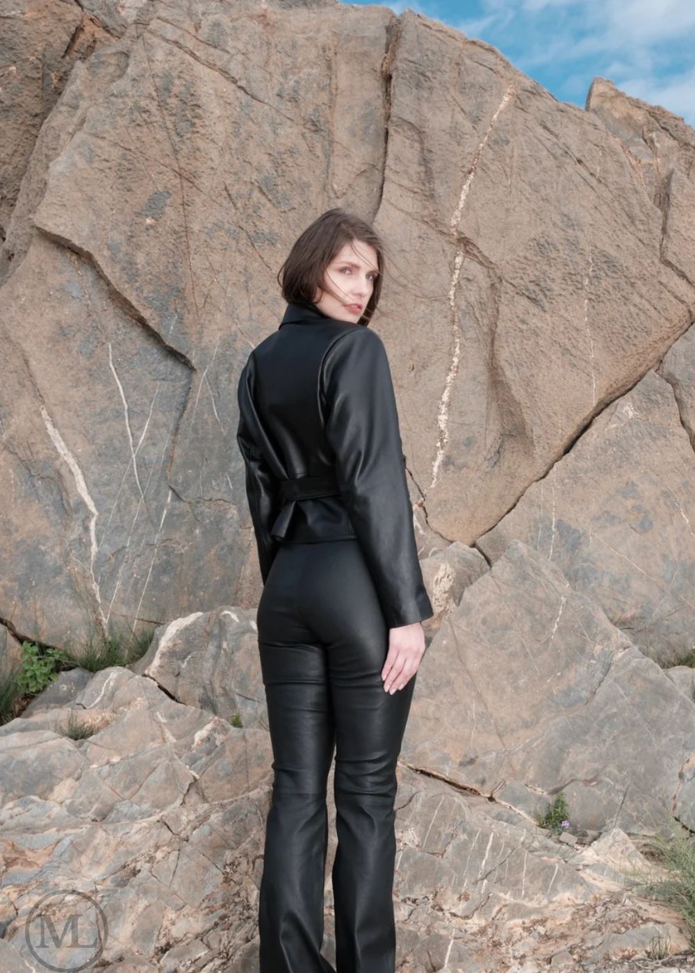 Woman wearing a black leather Blazer Coat outfit standing against rocky terrain with blue sky.