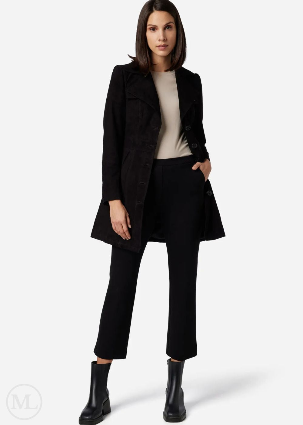 Femme portant un manteau noir, un pantalon noir et des bottes noires sur fond blanc