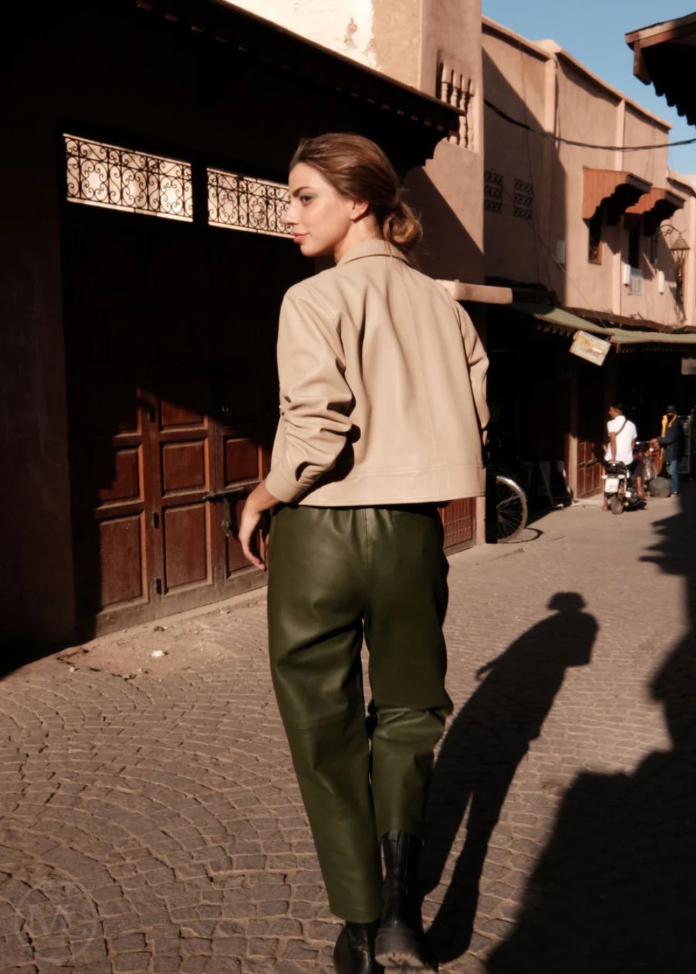 Woman walking on a street in an urban setting with buildings and people in the background.