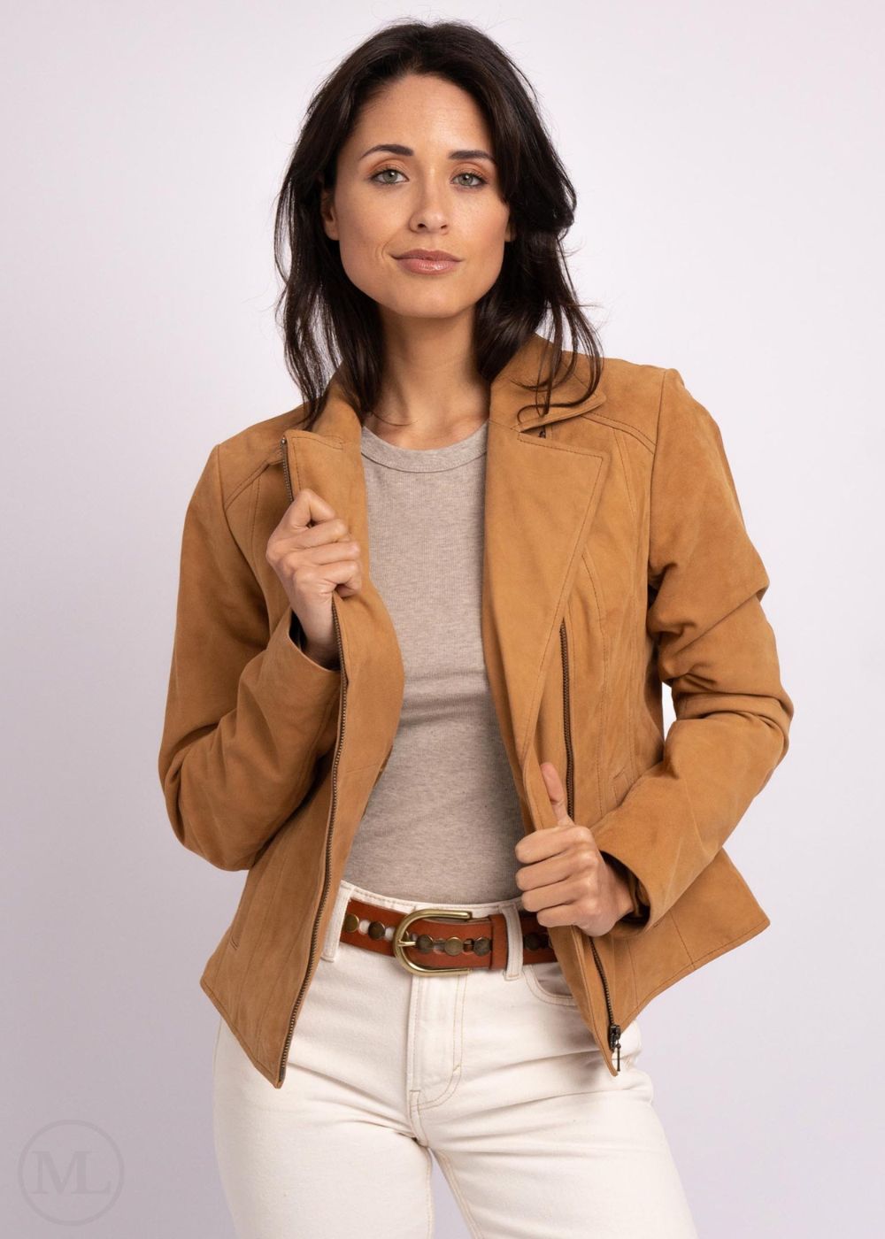 Woman wearing a camel leather jacket, gray shirt, and white pants on a light purple background