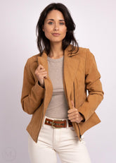 Woman wearing a camel leather jacket, gray shirt, and white pants on a light purple background