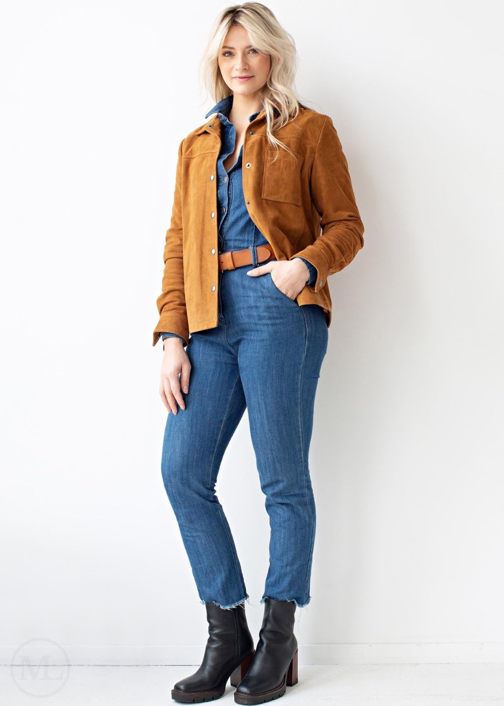 Woman wearing a cognac brown jacket, blue shirt, jeans, and black boots against a white background