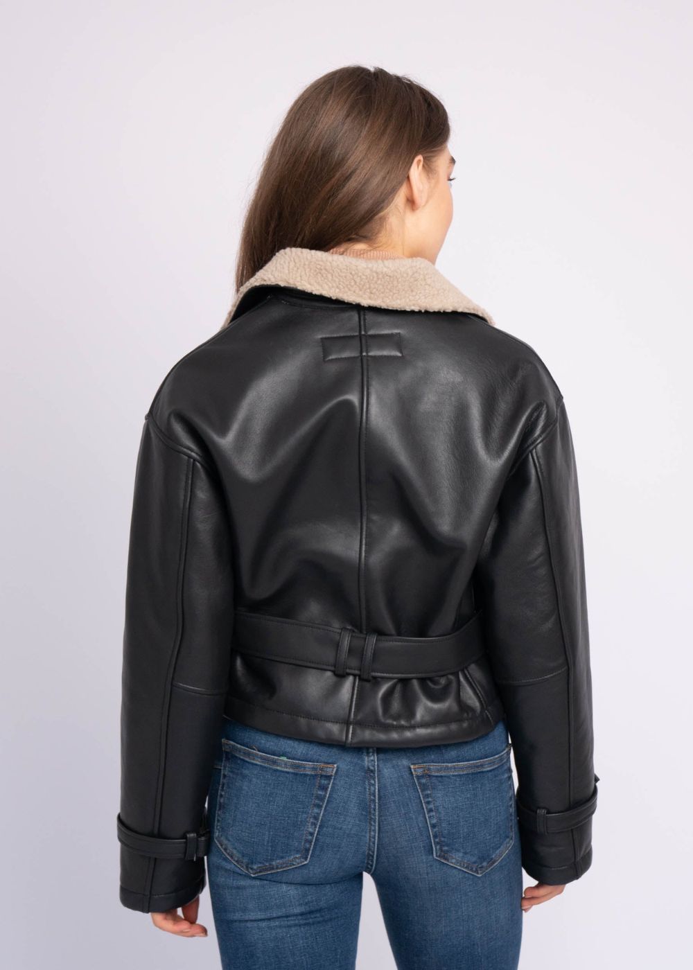 Person wearing a black aviator leather jacket with beige shearling collar on a white background