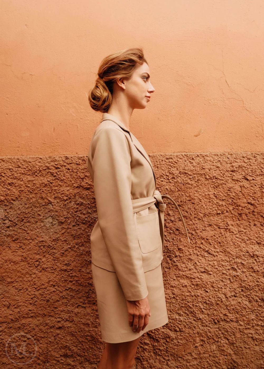 Woman in a leather blazer coat standing against a textured wall.