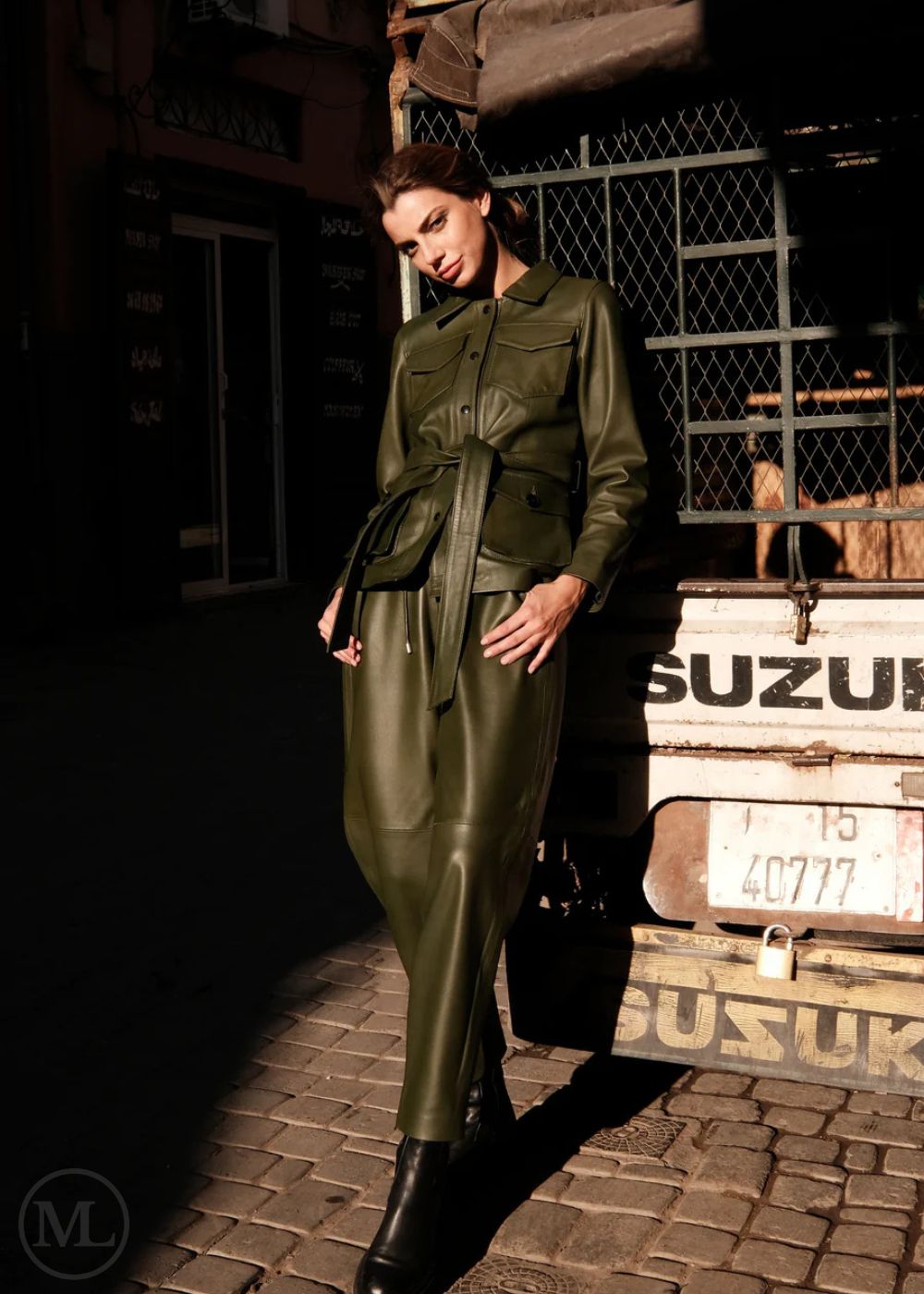 Woman in a olive khaki outfit standing next to a vintage Suzuki truck on a street.