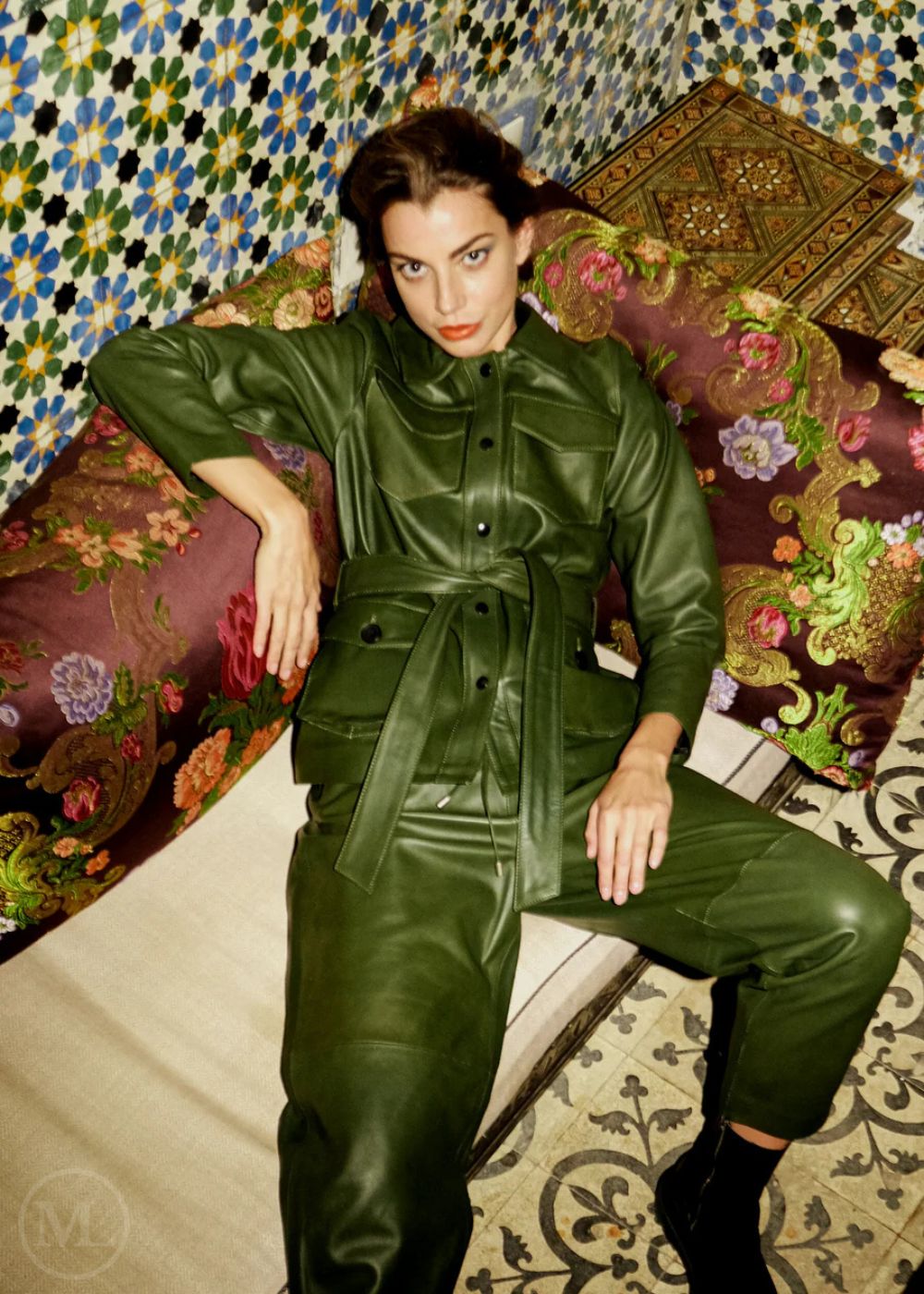 Woman wearing a olive khaki leather coat outfit sitting on a patterned couch.