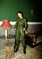 Woman in a green jumpsuit standing in a room with decorative walls and furniture.