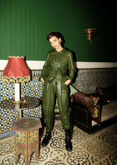 Woman in a green jumpsuit standing in a room with decorative walls and furniture.