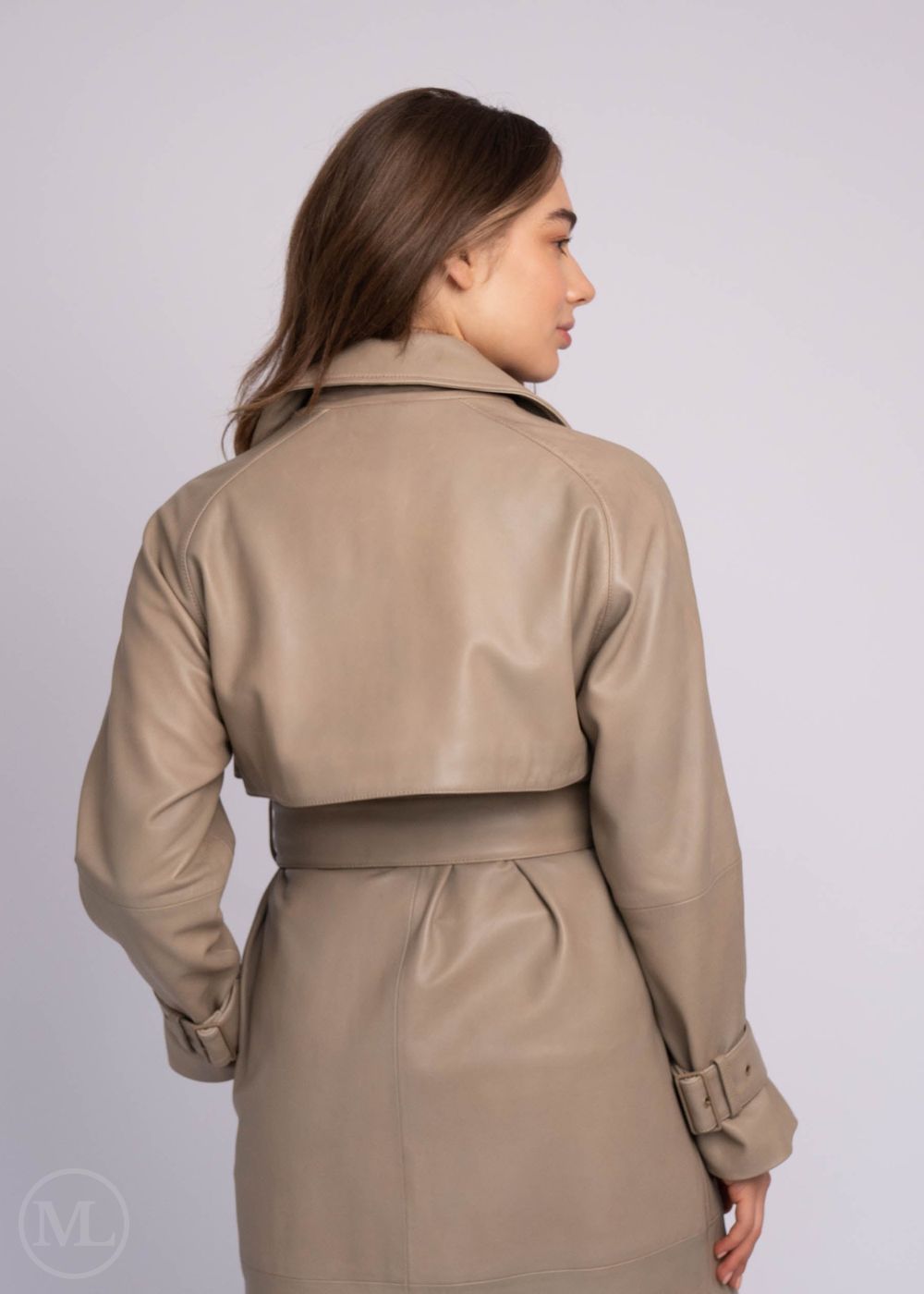 Woman wearing a taupe leather trench coat on a plain background
