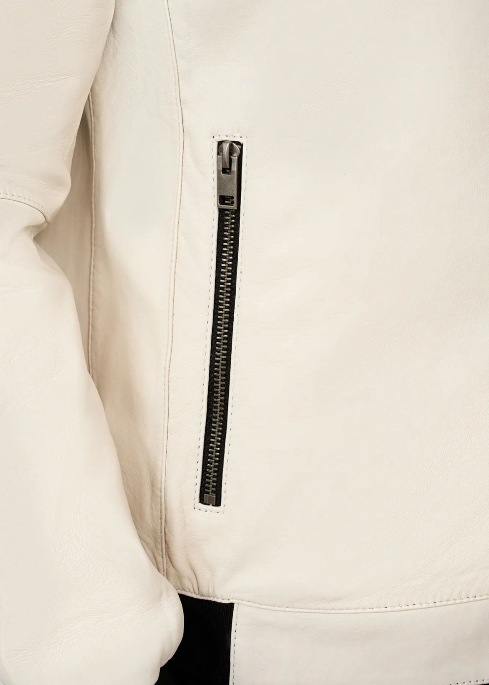 Close-up of a white leather bomber jacket with a black zipper on a light beige background