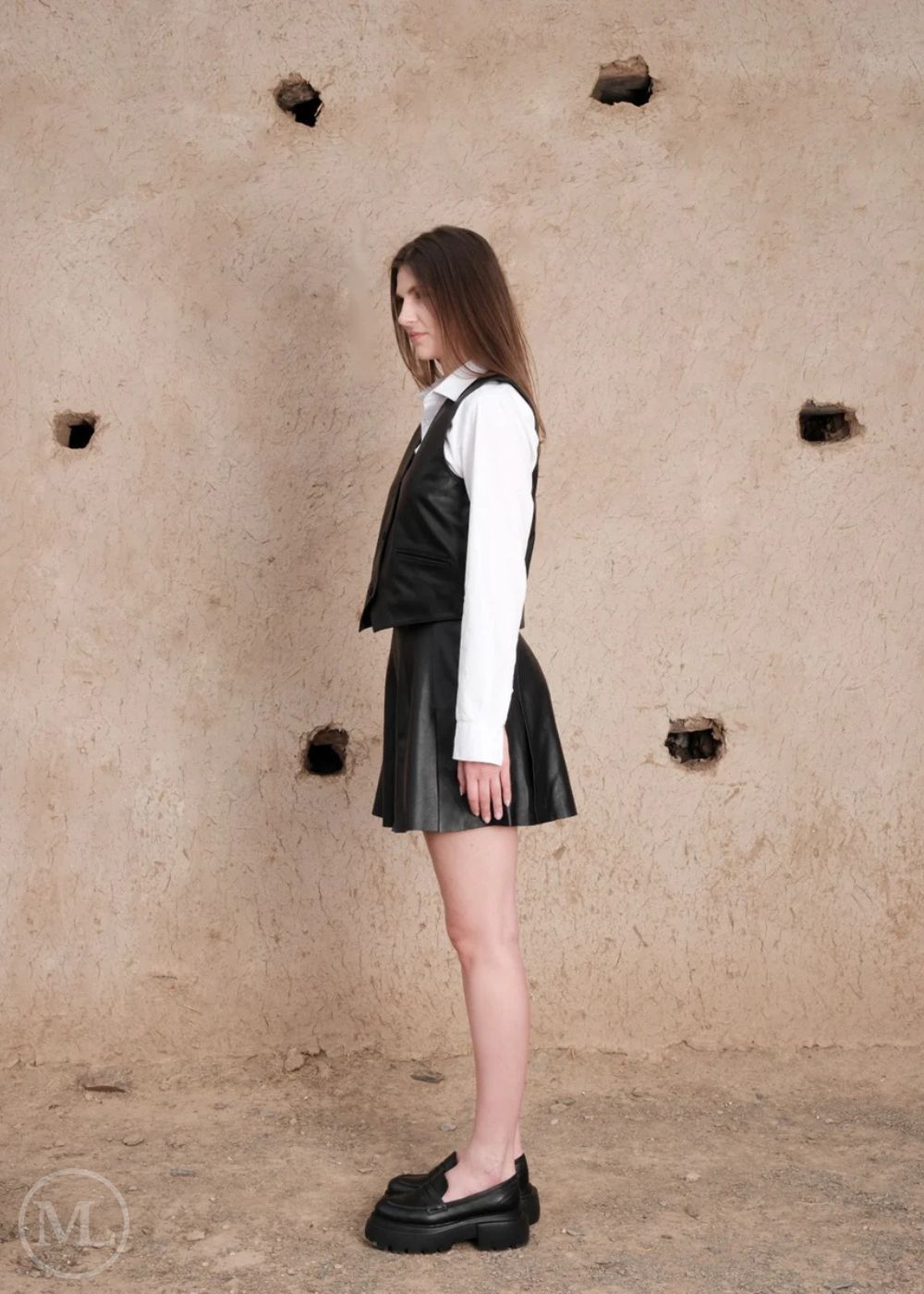 Woman wearing a black leather vest outfit against a textured beige wall