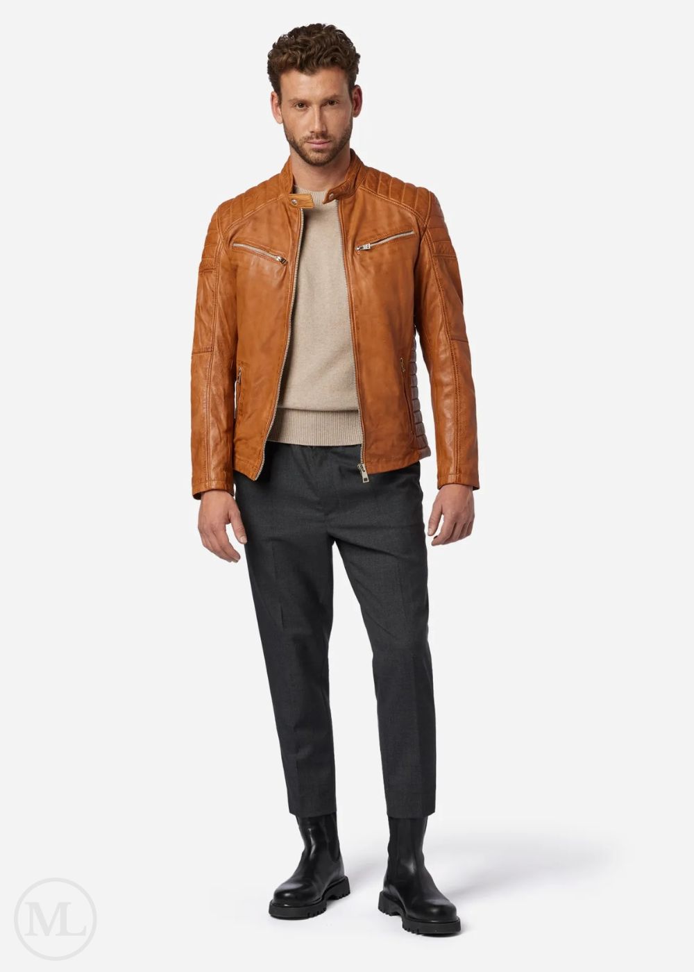 Man wearing a cognac brown leather biker jacket, beige sweater, black pants, and black shoes on a white background