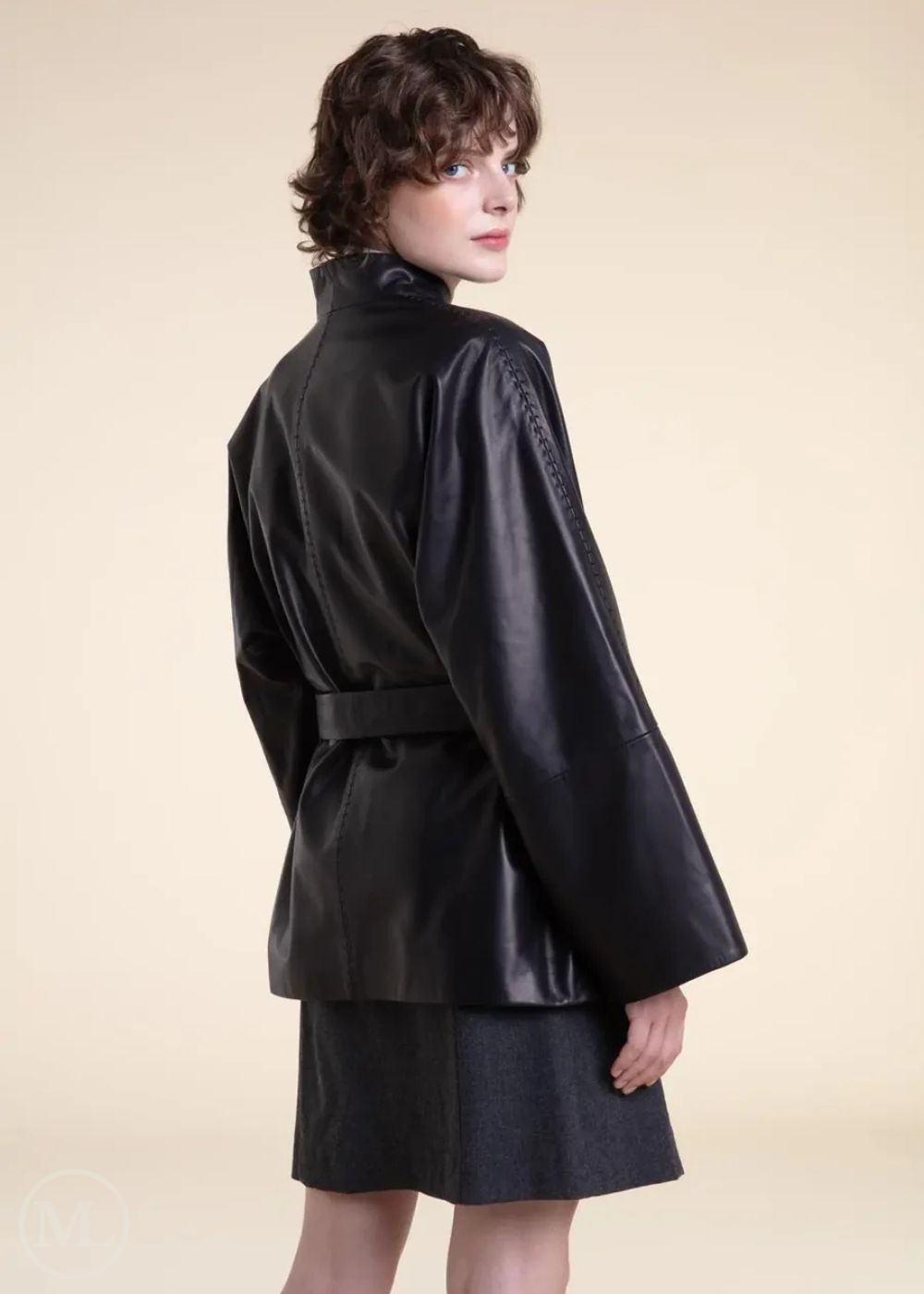 Woman wearing a black belted wrap leather blazer coat on a beige background