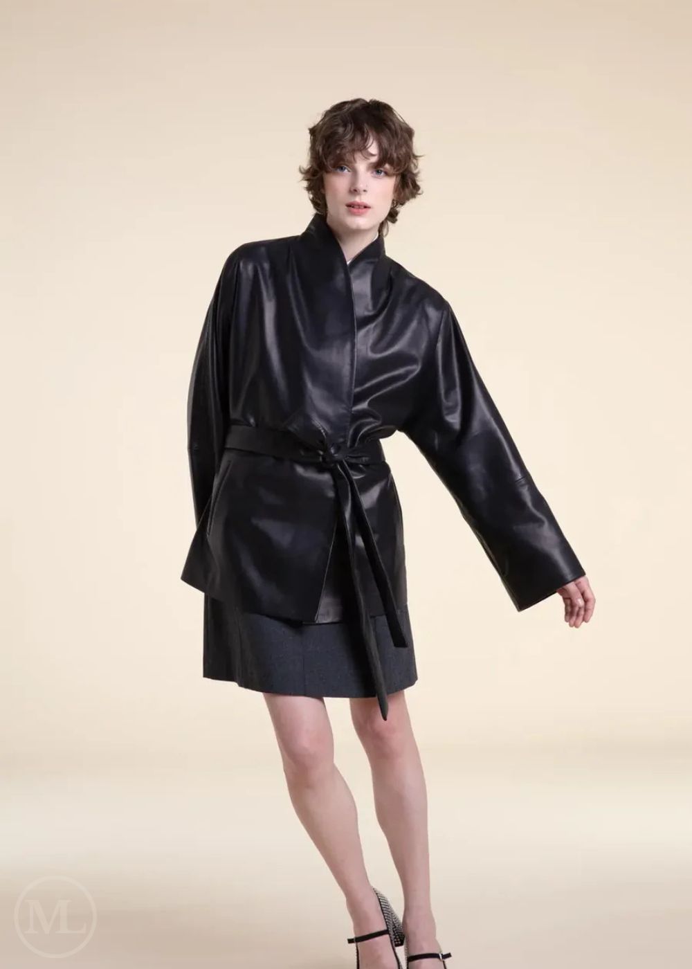 Woman wearing a black belted wrap leather blazer coat on a beige background