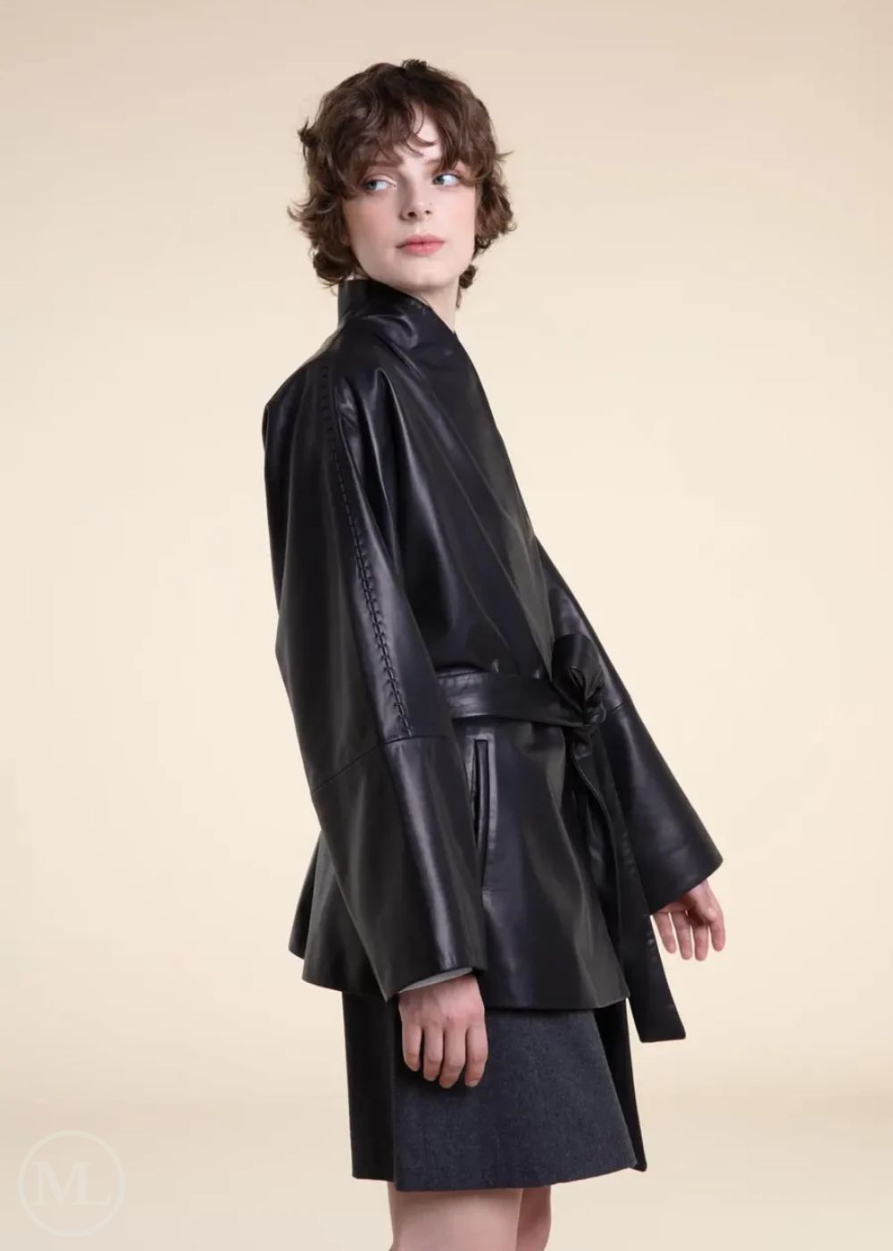 Women wearing a black belted wrap leather blazer coat on a beige background