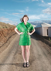 Woman in a green leather biker dress standing on a dirt road with a scenic background
