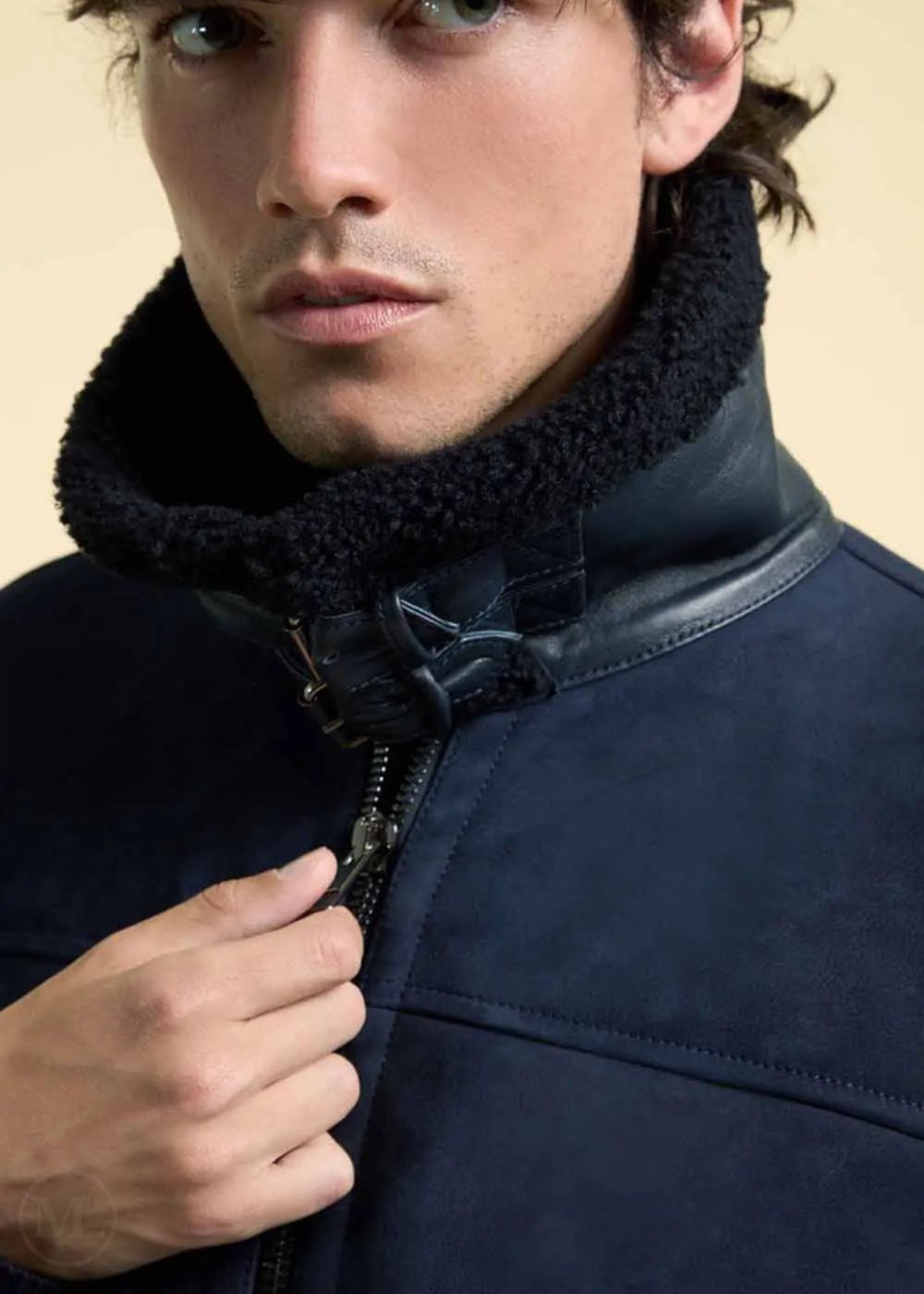 Man wearing a navy blue suede jacket with a black fur collar against a beige background