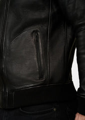 Close-up of a black leather bomber jacket with a zipper pocket worn by a man on a white background