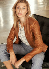 Woman wearing a cognac brown leather jacket sitting on a black chair.