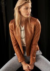 Woman wearing a cognac brown leather jacket sitting against a black background