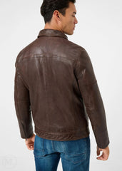 Man wearing a dark brown leather racer jacket and blue jeans on a white background