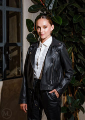 Women wearing a black leather biker jacket and white shirt standing against a plant backdrop