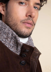 Close-up of a man wearing a dark brown jacket with a knitted scarf against a beige background