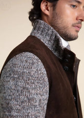 Man wearing a dark brown jacket over a gray sweater with a neutral background