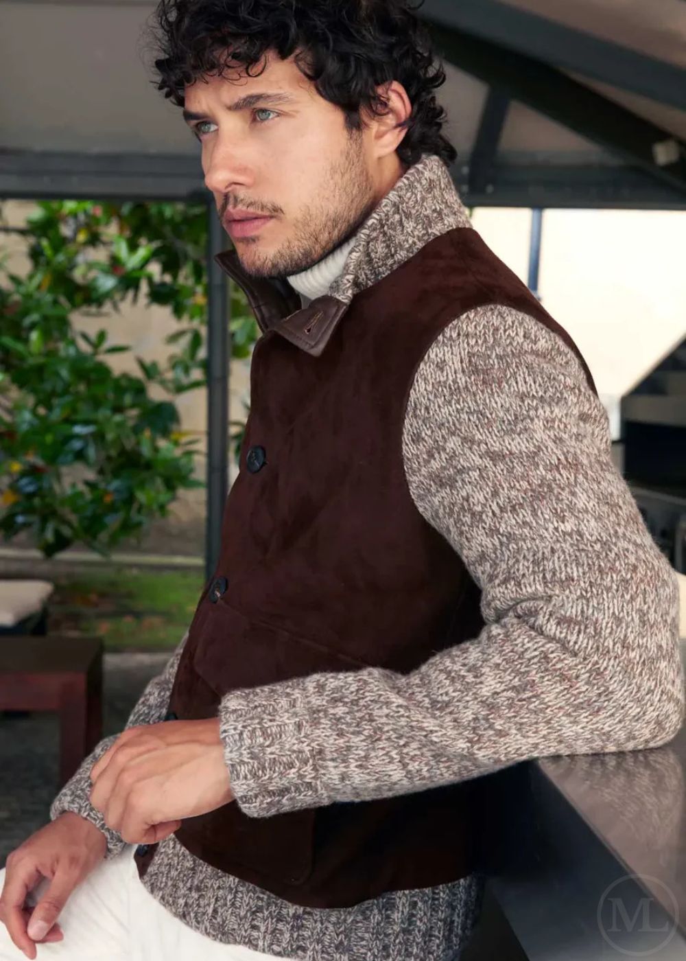 Man wearing a dark brown jacket over a gray sweater in an outdoor setting