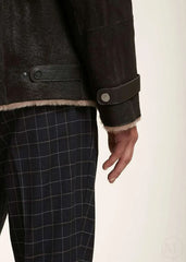 Close-up of a dark brown jacket with fur trim and checkered pants worn by a man on a plain background