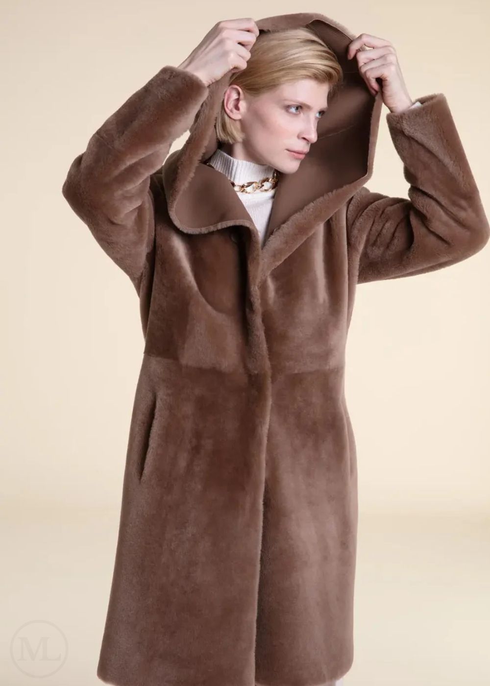 Woman wearing a beige shearling leather coat with a hood against a beige background