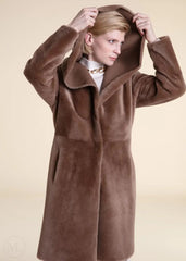 Woman wearing a beige shearling leather coat with a hood against a beige background