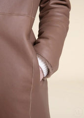 Close-up of a beige shearling leather coat worn by a woman with a beige background
