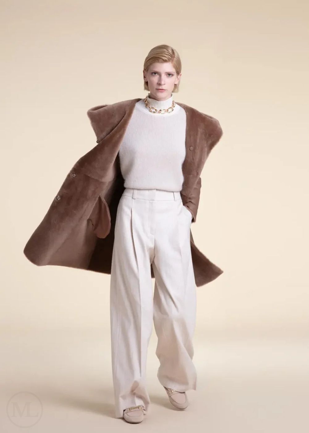 Woman wearing a beige shearling leather coat over a white outfit on a beige background