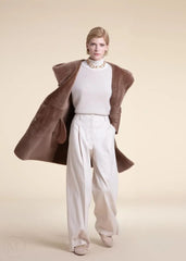 Woman wearing a beige shearling leather coat over a white outfit on a beige background