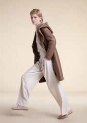 Woman wearing a beige shearling leather coat and white pants on a beige background