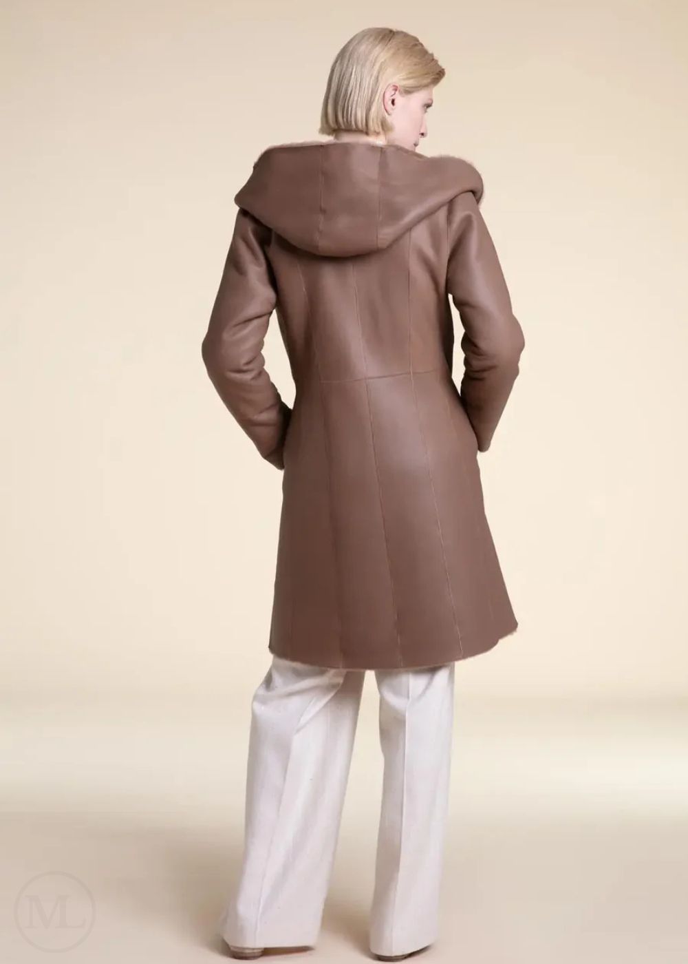 Woman wearing a beige shearling leather coat with a hood on a beige background