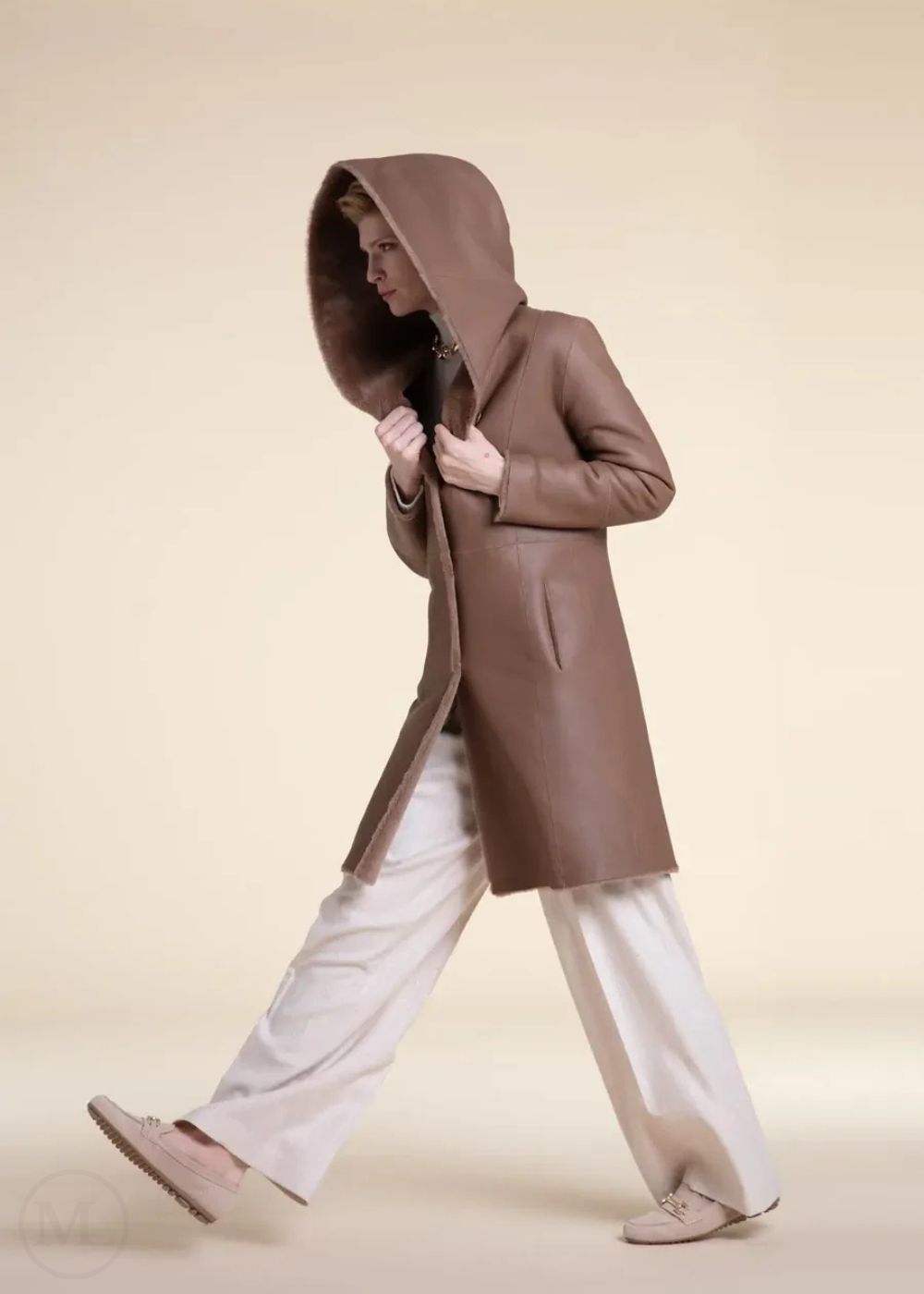 Woman wearing a beige shearling leather hooded coat on a beige background