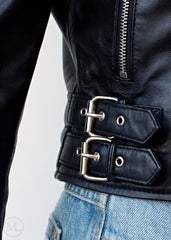 Close-up of a black leather biker jacket with a belt and silver buckles on a light gray background.